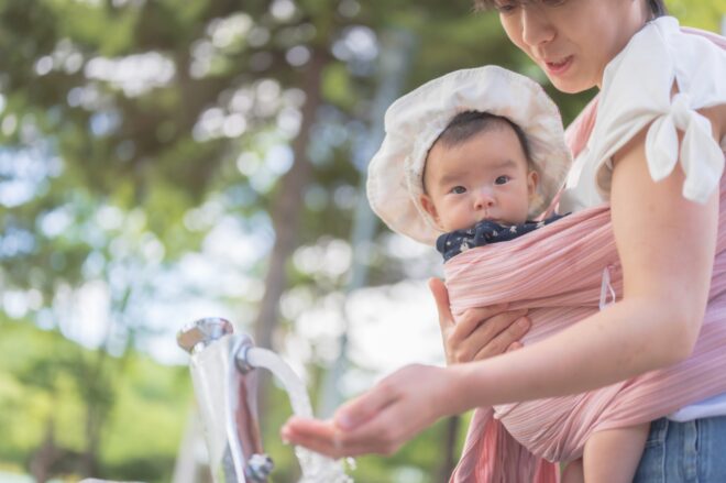 抱っこ紐とベビーカーを持って赤ちゃんとおでかけしている母親のイメージ